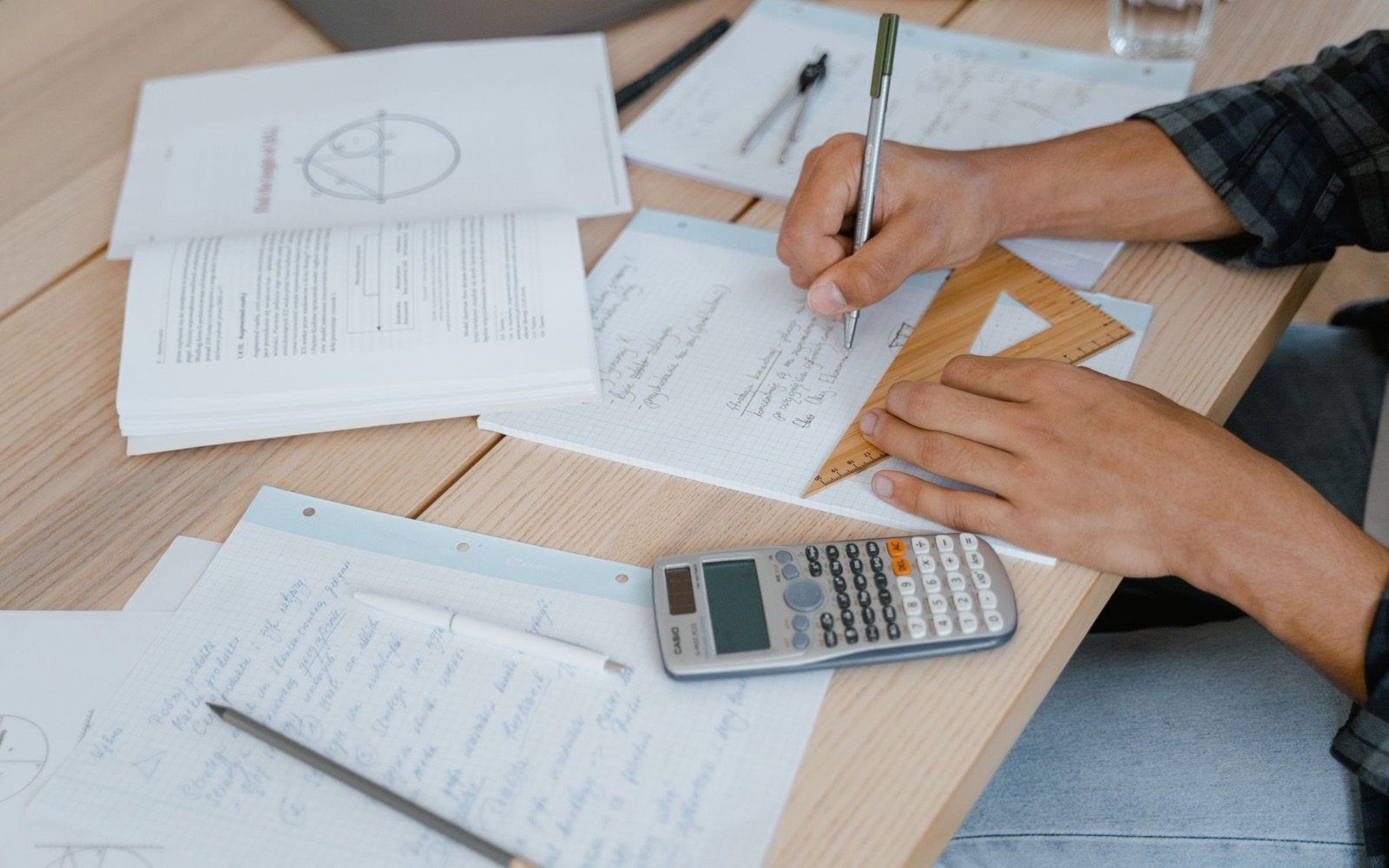 A student working through maths problems with a calculator and a set square