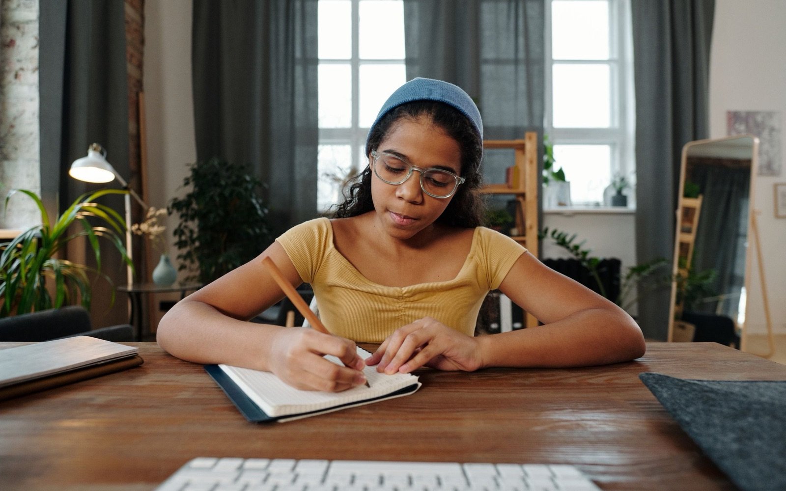 A teenage student in glasses writing carefully in her notebook at a desk