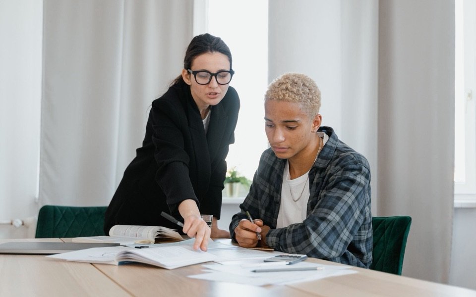 A university counsellor guiding a student through his plans at a table